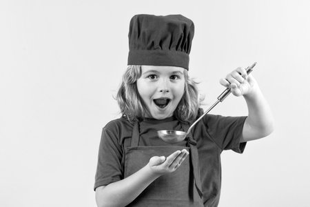Funny kid chef cook with kitchen ladle, studio portrait. Cooking children. Chef kid boy making healthy food. Portrait of little child in chef hat isolated on studio background.の写真素材