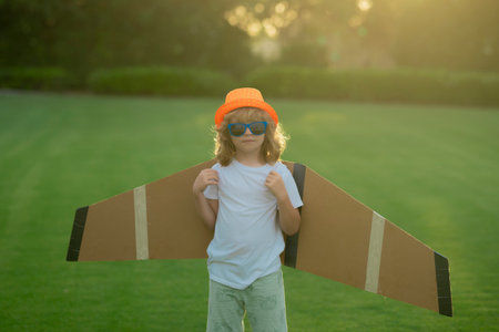 The concept of child kindness and childhood. Pilot aviator child with a toy airplane plays on summer nature. Child playing with plane wings. Concept of dreams and travels.の写真素材