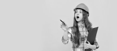 Renovation child, shocked teen girl in helmet and checkered shirt making notes on clipboard, working. Child in hard hat horizontal poster design. Banner header, copy space.の写真素材