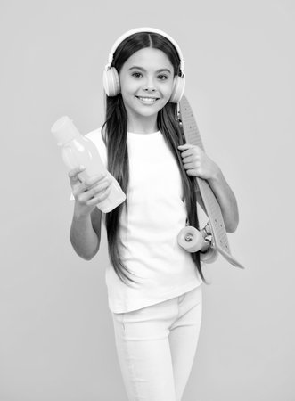 Happy teenager portrait. Teen hipster girl skater with skateboard and headphones on isolated background. Summer kids trend, urban teenage style. Smiling girl.の写真素材