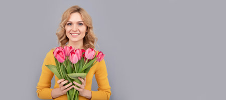 positive girl hold flowers for spring holiday on grey background. Woman isolated face portrait, banner with mock up copy space.の写真素材
