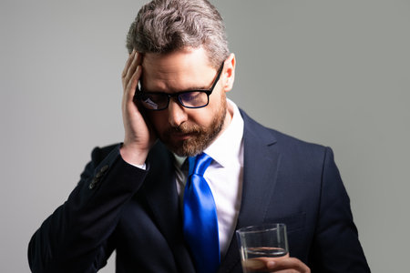 Sad man got migraine touches her head because of pain. Man in suit with headache isolated on gray studio. Freelancer or manager with headache. Stressed, tired business man from headache.の写真素材