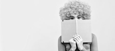 Bookworm in training. Funky bookworm yellow background. Happy kid cover face with book. Funny teenager child on party, poster banner header with copy space.の写真素材