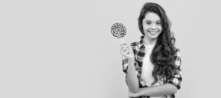 yummy. happy girl hold lollipop. lollipop child. hipster kid with long curly hair hold lollypop. Teenager child with sweets, poster banner header, copy space.の写真素材