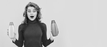 surprised redhead girl curly dyed hair choosing body care product of shampoo bottle, hairdresserの写真素材