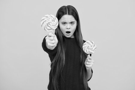Hipster teenager child girl lick lollypop. Sugar nutrition, candy and sweets. Child eat lollipop . Angry teenager girl, upset and unhappy negative emotion.の写真素材