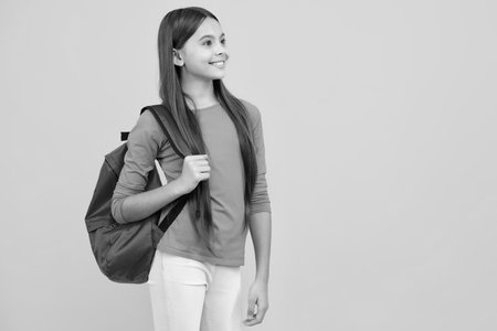 School girl in school uniform with school bag. Schoolchild teenager hold backpack on yellow isolated background. Happy teenager portrait. Smiling girl.の写真素材