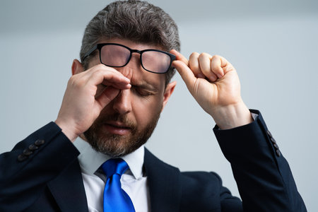 Stressed business man in suit having headache. Tired businessman is working overtime and has headache. Overworked man suffers from headache. Migraine from overwork, deadline, difficult at work.の写真素材