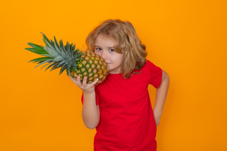 Healthy fruits for kids. Kid with pineapple in studio. Studio portrait of cute child hold pineapple isolated on yellow background.の写真素材