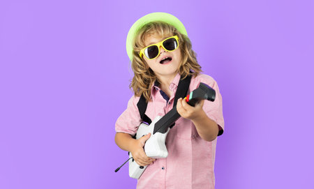 Portrait of little boy in pink sunglasses playing electric guitar. Cute child boy sings and plays on...