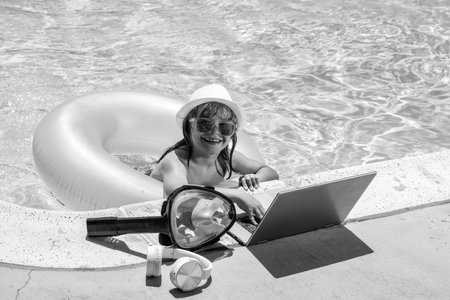 Child working on laptop computer at swimming pool. Summer online technology. Traveler relaxing on tropical water in summer holidays vacation. Travel trip, kid using laptop.の写真素材