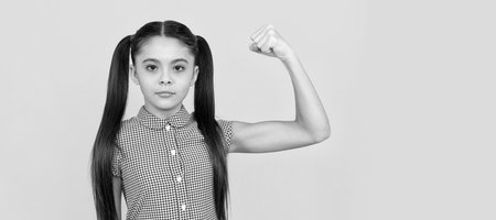 Serious girl child show power gesture flexing arm yellow background, strong. Child face, horizontal poster, teenager girl isolated portrait, banner with copy space.の写真素材