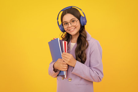 School child girl with headphones and book isoalted on yellow background.