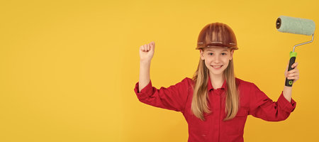 glad teen child in builder hard hat with paint roller on yellow wall. Child builder in helmet horizontal poster design. Banner header, copy space.の写真素材