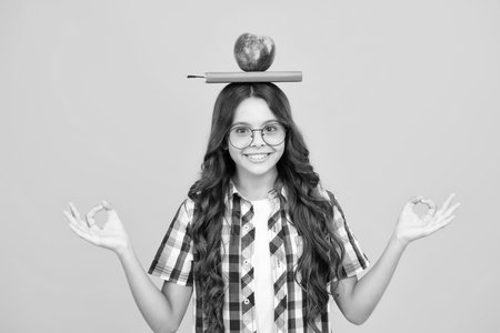 Back to school. Teenager schoolgirl with bag hold apple and book, ready to learn. School children on isolated yellow background.の写真素材