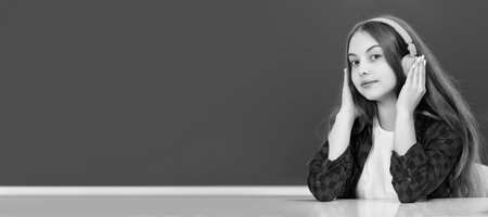 smiling kid with earphones at blackboard, audio accessory. Banner of schoolgirl student. School child pupil portrait with copy space.の写真素材