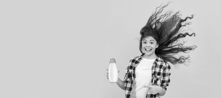 kid use shower gel. happy teen girl with shampoo bottle. shampooing hair in salon. Banner of child girl hair care, studio poster header with copy space.の写真素材