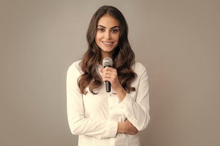 Beautiful business woman is speaking on conference. Stylish girl singing songs with microphone, holding mic at karaoke, posing against gray background.の写真素材