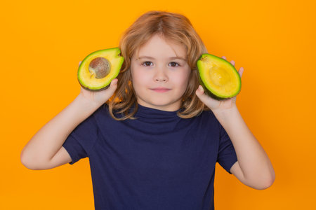 Vitamin and healthy fruits for kids. Kid hold red avocado in studio. Studio portrait of cute child with avocado isolated on yellow background, copy space.の写真素材