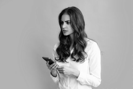 Serious business woman looking at the phone screen, reading message on smartphone, typing text on smart mobile phone. Female freelancer chatting by mobile phone.の写真素材