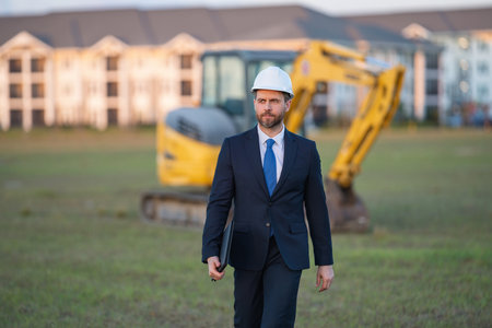 Buider man in suit and hardhat. Construction investor. Business man investor in front of construction site. Successful investor. Handsome man in suit and hardhat at building construction.の写真素材