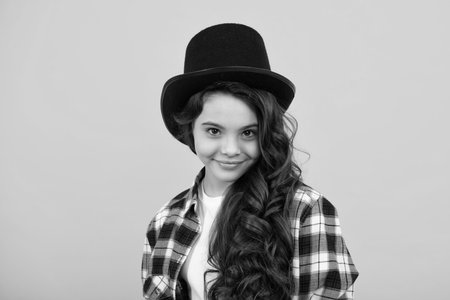 Child teen girl in magician hat, cylinder hat isolated on yellow background. Headwear. Clothes accessories. Fashion headwear for gentlemen in vintage style, old classic cylinder.の写真素材