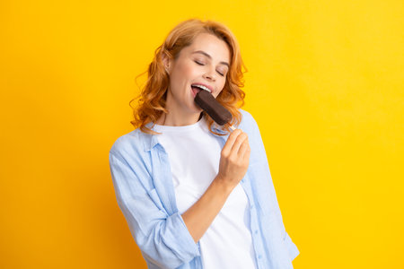 Summer concept. Glad positive woman holds tasty frozen ice cream, enjoys eating delicious cold dessert, poses on yellow background, feels happy.の写真素材