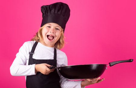 Child chef cook with pan. Child chef cook. Child wearing cooker uniform and chef hat preparing food, studio portrait.の写真素材