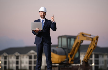 Buider man in suit and hardhat. Construction investor. Business man investor in front of construction site. Successful investor. Handsome man in suit and hardhat at building construction.の写真素材