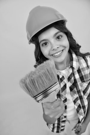 Teenager child painter in helmet with painting brush. Child in hard hat. Kid builder painter on construction site. Renovation and repair.の写真素材