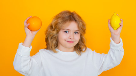 Kid with orange and lemon in studio. Studio portrait of cute child hold lemon and orange isolated on yellow background.の写真素材