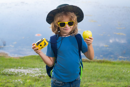 Child with camera travelling outdoors. Boy traveler with backpack in a summer day. Portrait of a little boy exploring wildlife. Hiking and adventure concept.の写真素材