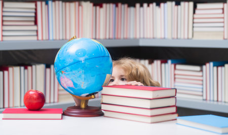 School boy looking at globe in library, geography lesson. School child student learning in class, study english language at school. Elementary school child. Portrait of funny pupil learning.の写真素材