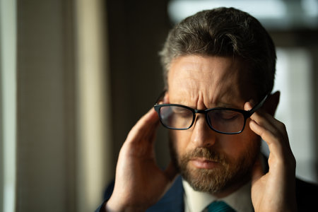 Headache, tiredness and stress. Business man in suit uses a laptop, is tired got headache migraine. Headache pain concept. Painful men are stressed at work in office. Stressful and headache.の写真素材