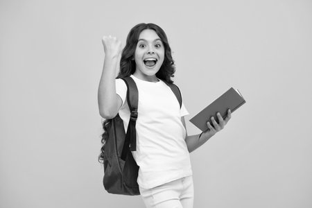 Amazed teen girl. Back to school. Teenager school girl hold book and copybook ready to learn. School children with school bag on isolated yellow studio background. Excited expression, cheerful and glad.の写真素材