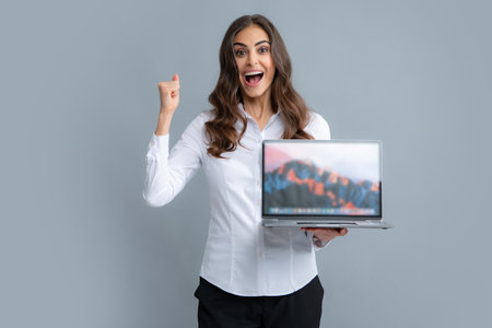 Portrait of a cheerful young casual girl standing isolated over gray background, using laptop computer. Business woman at work.の写真素材