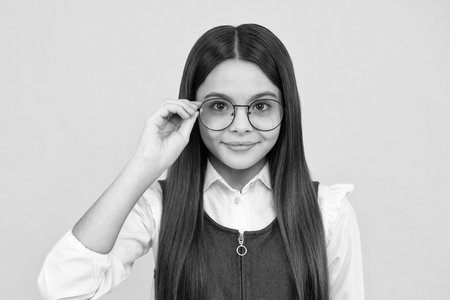 Headshot portrait of cute teenager child girl isolated on yellow studio background wear glasses look at camera, kid eyesight treatment concept. Happy girl face, positive and smiling emotions.の写真素材