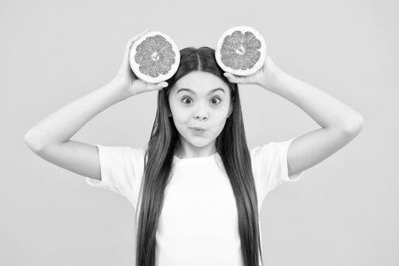 Teenage girl holding a grapefruit on a yellow background. Funny face.の写真素材