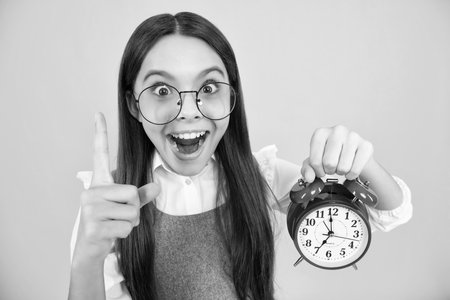 Portrait of teenage girl with clock alrm, time and deadline. Studio shot isolated on yellow background. Surprised teenager girl.の写真素材