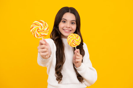 Teen girl hold lollipop caramel on yellow background, candy shop. Teenager with sweets suckers. Happy face, positive and smiling emotions of teenager girl.の写真素材