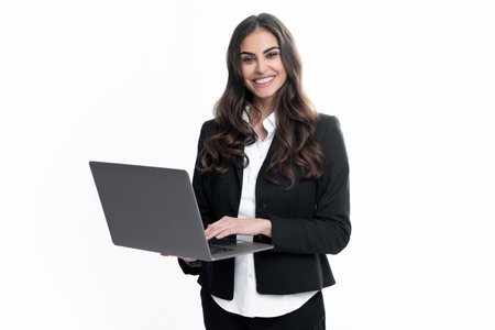 Portrait of a cheerful young casual girl standing isolated over gray background, using laptop computer. Business woman at work.の写真素材