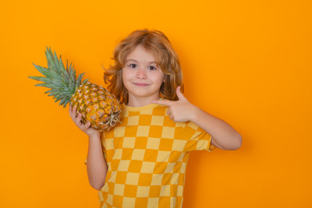 Kids face with fruits. Kid with pineapple in studio. Studio portrait of cute child hold pineapple isolated on yellow background.の写真素材