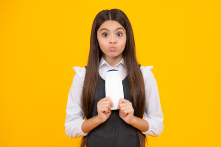 Funny face. Teenager child girl showing bottle shampoo conditioners or shower gel. Hair cosmetic product. Bottle for advertising mock up copy space.の写真素材