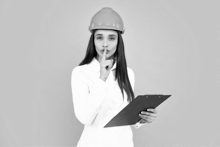 Serious woman in protective helmet with clipboard isolated on grey background. Young woman construction manager. Architect woman, female worker in hardhat helmet.の写真素材