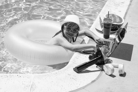 Child working on laptop computer at swimming pool. Summer online technology. Traveler relaxing on tropical water in summer holidays vacation. Travel trip, kid using laptop.の写真素材