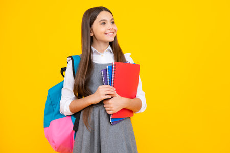School girl hold copybook and book on yellow isolated studio background. School and education concept. Teenager girl in school uniform.の写真素材