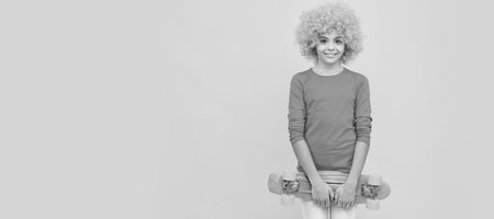 cheerful selfish child girl in curly wig hold penny board, copy space, childhood. Funny teenager child on party, poster banner header with copy space.の写真素材