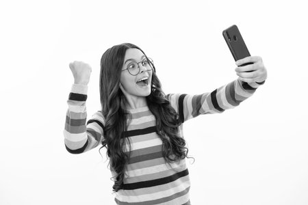 Kids selfie. Portrait of excited teenage girl using mobile phone, chatting on web, typing sms message. Mobile app for smartphone.の写真素材