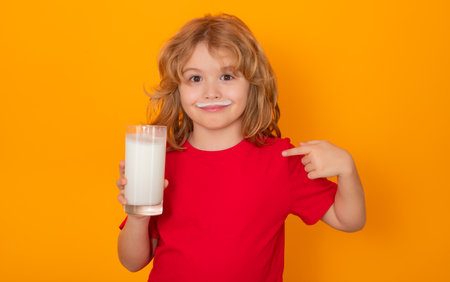 Kid drink fresh milk. Funny blonde child drinking milk isolated on yellow. Little boy with milk mustache hold glass of milk.の写真素材