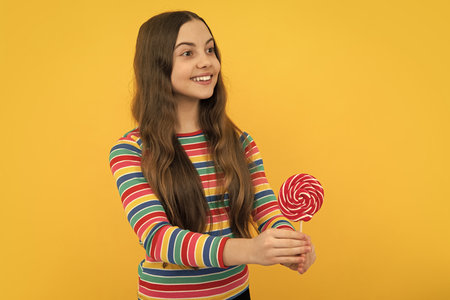 Cool teen child with lollipop over yellow isolated background. Sweet childhood life. Teen girl with yummy lollipop candy.の写真素材